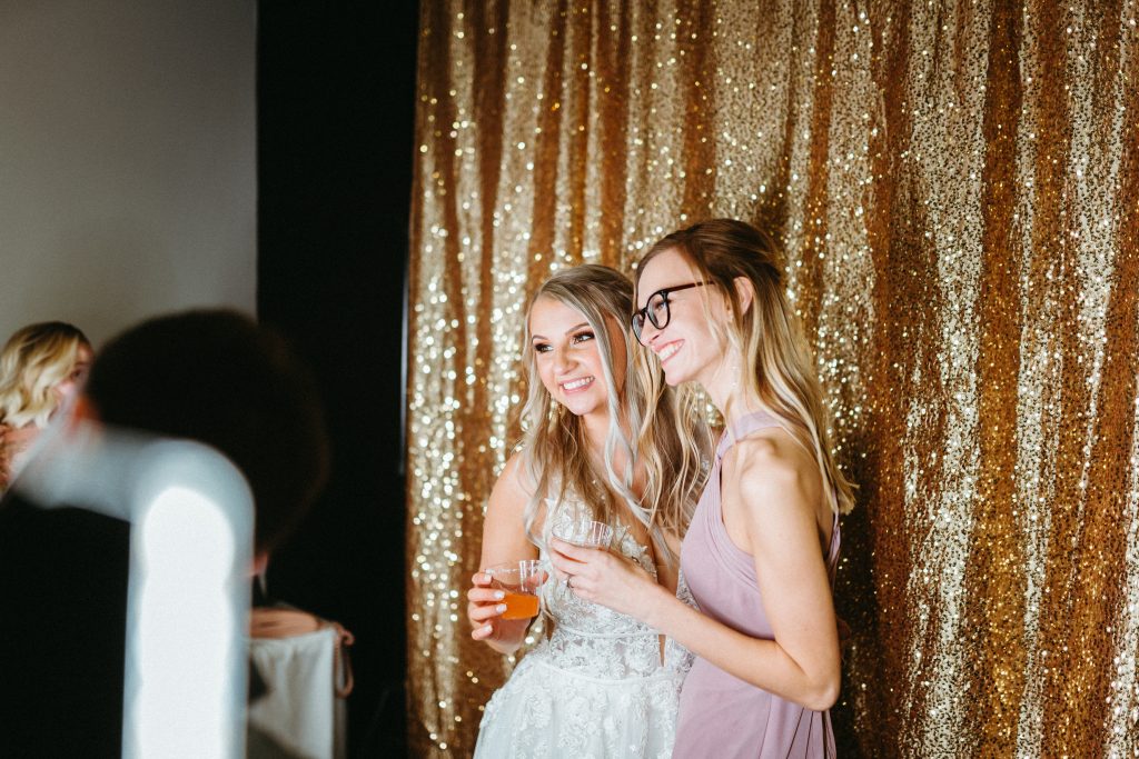 a bride and bridesmaid at a wedding at Kindred Barn stand in front of Northwest Arkansas Photo booth and take a photo together