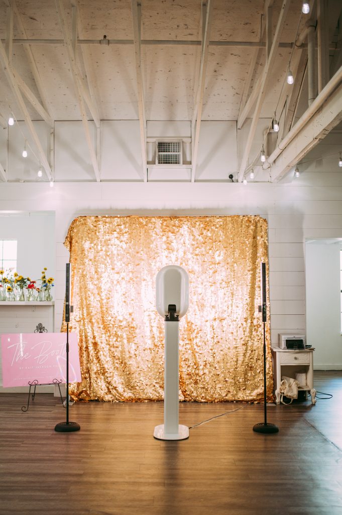 NWA Photo Booth is using extra lighting to make sure the images taken are of the highest quality possible. This image of the photo booth rental was taken at a wedding at Kindred North in Centerton, Arkansas with a gold sequin backdrop and printer.