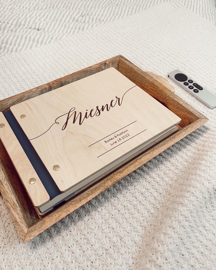 NWA Photo Booth has a wooden guest book laid on the bed. It holds white cardstock paper inside that guests place their photo strips in and write notes on.