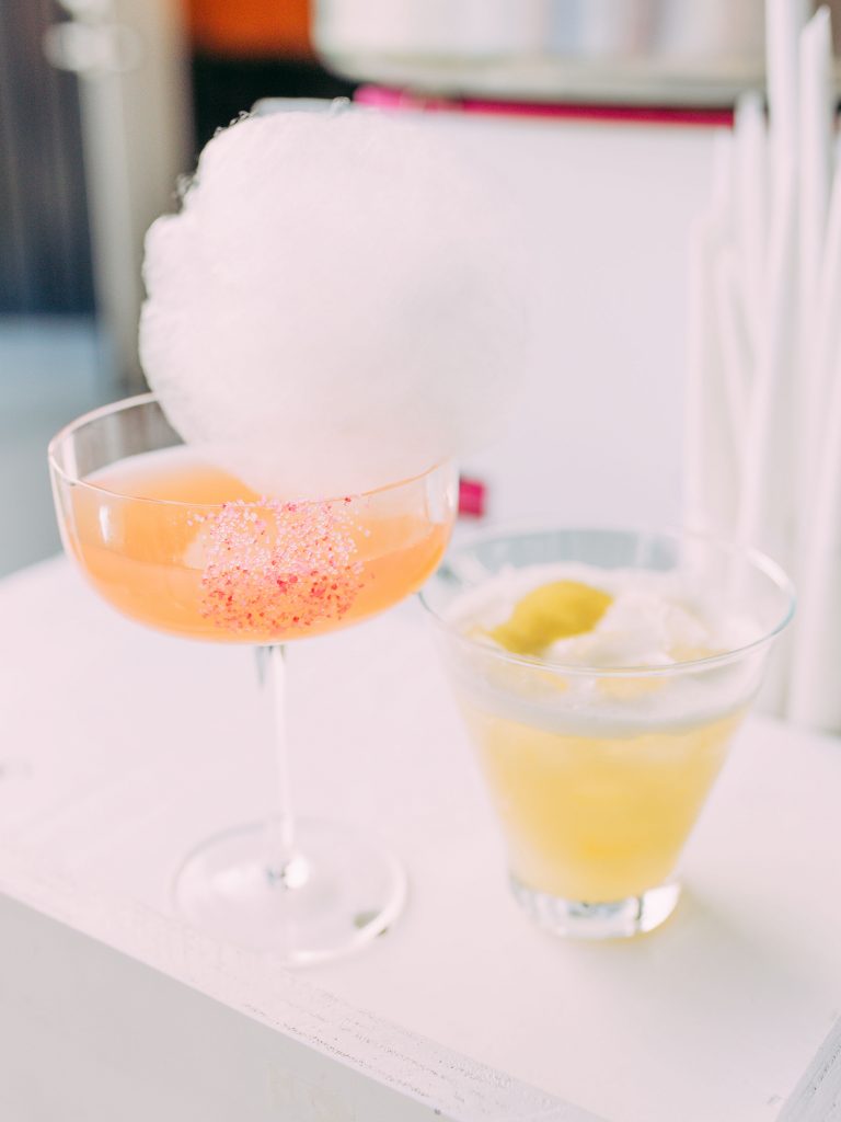 This is an image shot By Christi Musial Photography, a Northwest Arkansas Wedding Photographer. The image is a close up of a delicious cocktail by Mint 2 Mix, topped with a white cotton candy puff from lemon and puff. The rim of the glass has pink sugar crystals around it.